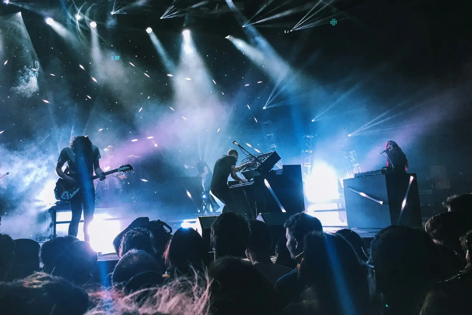 Band performing on a stage in front of an audience under blue and white stage lights