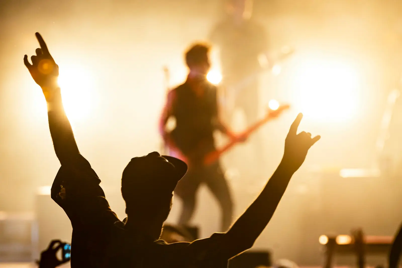 Concert crowd with raised hands in front of a band lit by warm stage lights