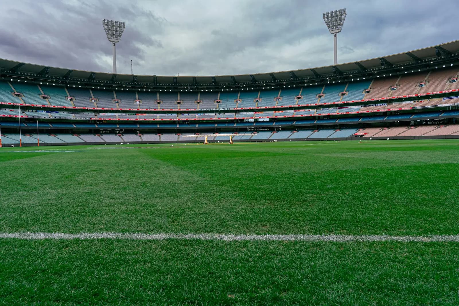 Sports ground with a green field, floodlights and empty stands under a cloudy sky
