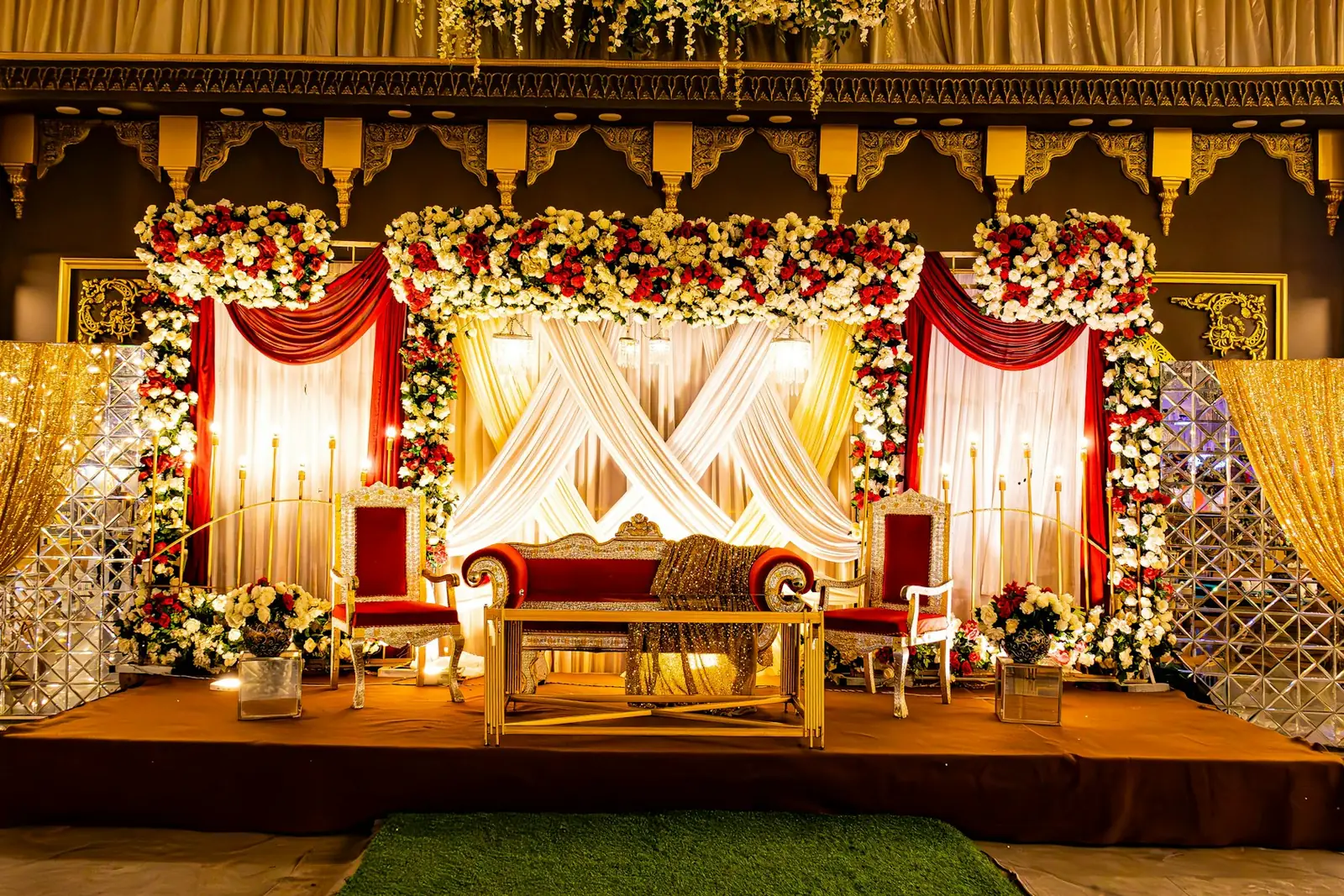 Decorated wedding stage with a red sofa, flower arches, draped fabric and gold panels