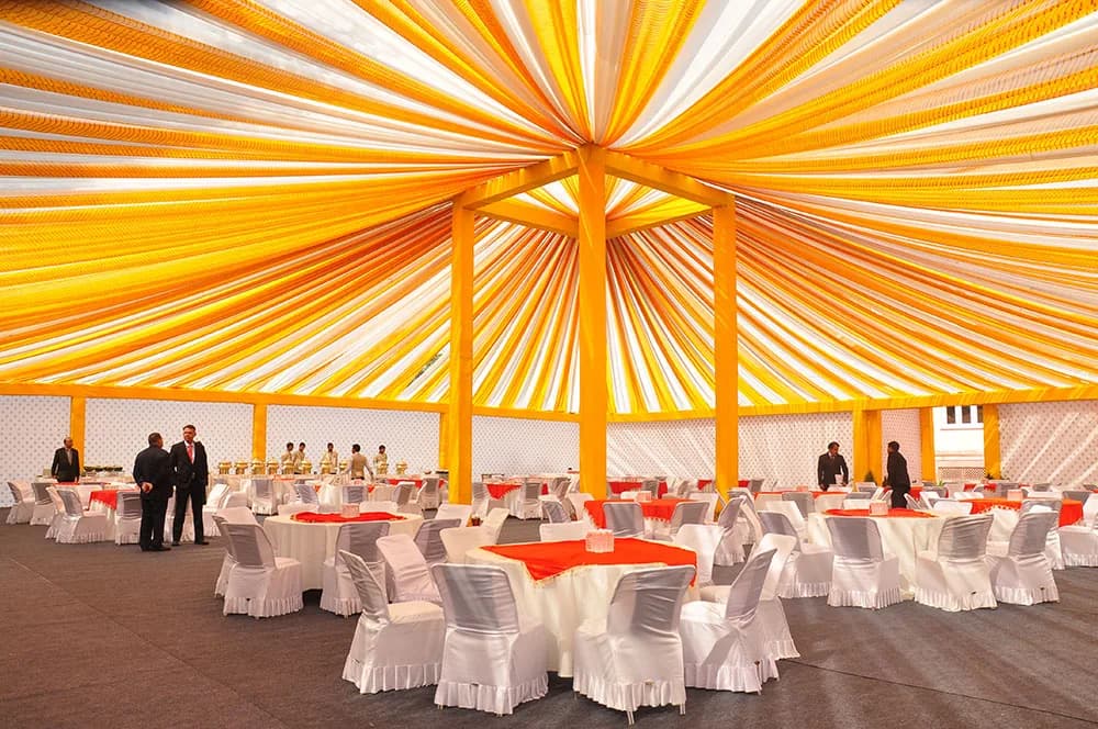 Orange and yellow fabric-draped tent with round dining tables set for guests